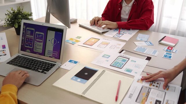 Excellent startup company employee presenting user interface prototype for mobile application to smart co-worker in office workspace. UX UI designer explain function of icon design on paper. Synergic
