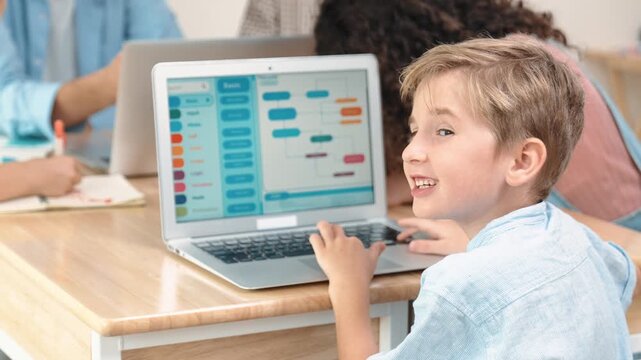 Smart caucasian boy turn around and looking at camera in STEM technology class while group of diverse student and teacher doing mind mapping. Smart child learning coding software program. Pedagogy.