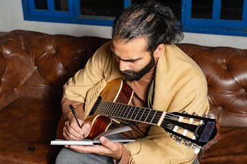 Person writing in notebook while holding guitar in cozy indoor setting.