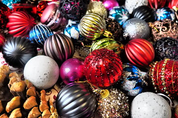 A vibrant collection of Christmas ornaments in various colors and textures, including shiny reds, greens, and golds, surrounded by pinecones, perfect for holiday cheer and New Year festivities