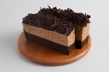 A layered chocolate brownie dessert on a wooden plate against a clean white background with a shallow depth of field.
