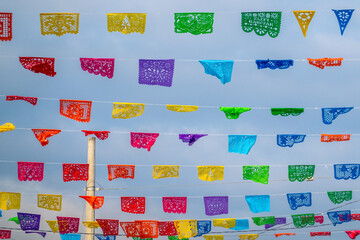 Vibrant, multicolored Mexican Papel Picado (perforated paper) banners strung overhead against a bright blue sky, commonly used for festivals in Huatulco, Oaxaca, Mexico.