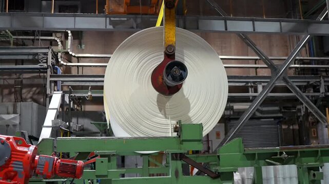 Large cellulose paper roll moving through industrial production line inside modern pulp and paper factory.
