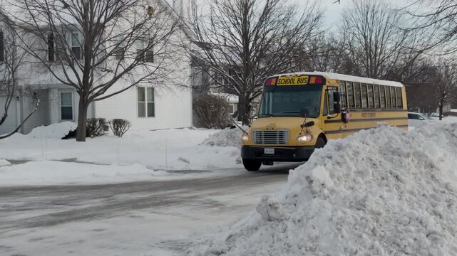 Yellow school bus navigating a suburban neighborhood covered in snow. Large snowbanks line the street as the bus makes its way through winter conditions. POV View