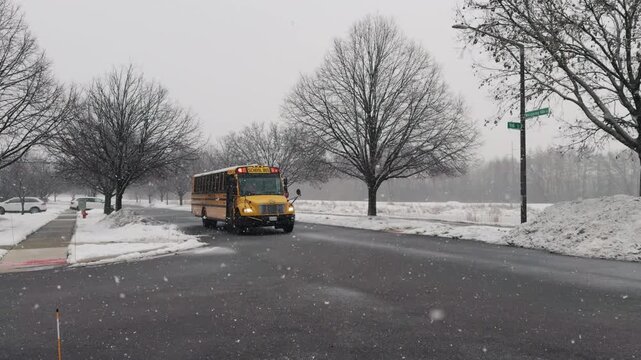 Yellow school bus stopping at suburban neighborhood during active snowfall. Snow blankets the ground as flakes fall steadily, creating a cold winter scene POV View