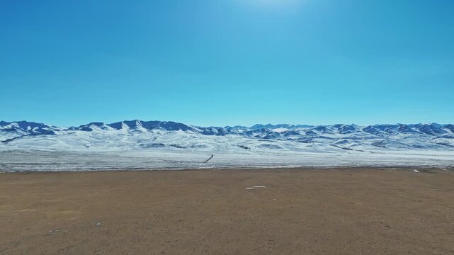 Qilian Grassland, Xining, Qinghai Province, China - A Vast, Barren Plain Leads to a Long Stretch of Snow-Covered Mountains Under a Clear Blue Sky - Push In Shot