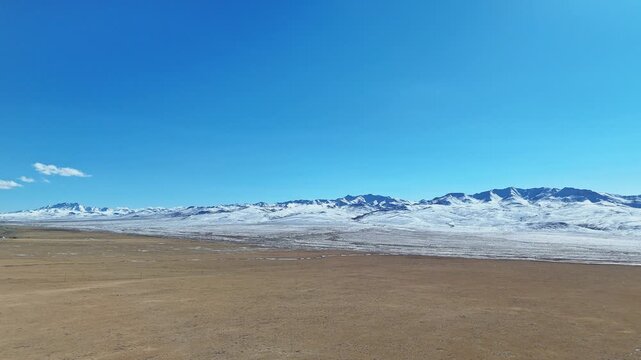 Qilian Grassland, Xining, Qinghai Province, China - A Vast, Barren Plain Stretches Toward Snow-covered Mountains Under a Clear, Expansive Blue Sky - Drone Flying Forward