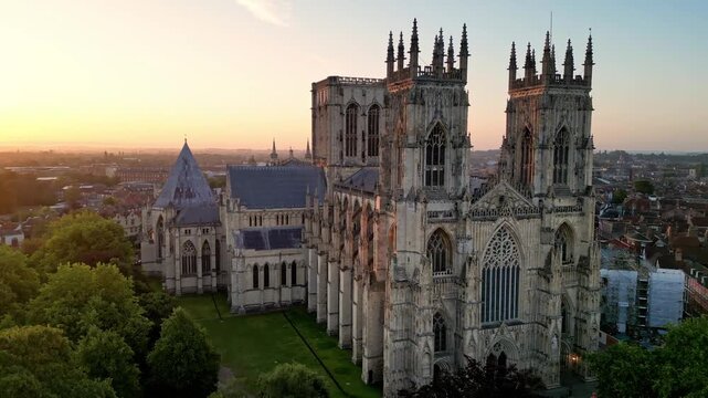 Aerial drone point of interest counter clockwise around the main entrance of York Minster, gradually revealing the sunrise and early morning light over the Gothic cathedral in York, England.