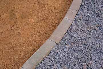 Abstract close-up of sidewalk construction materials. Sand, gravel, and concrete curb form contrasting textures and colors, showing road paving and urban infrastructure work.