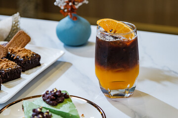 A glass of iced orange juice top up by americano coffee with a piece of sliced fresh orange in cafe