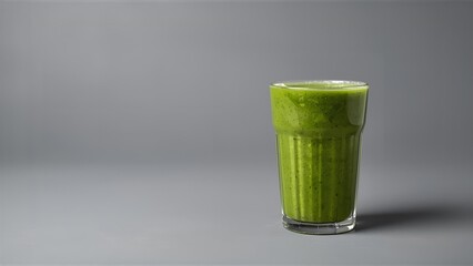 A studio shot showing a glass filled with a healthy green smoothie on a grey background.
