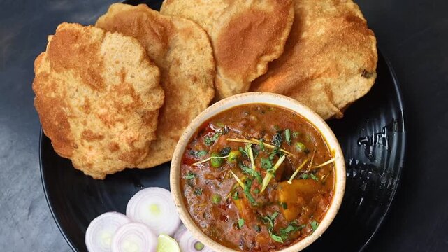 Puri sabzi on black plate with onion on the side