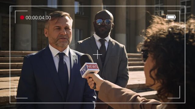 Medium shot with professional video camera frame effect of mature Caucasian male attorney with security detail answering questions from reporter on lawsuit on steps of court building