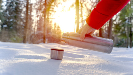 A man pours hot tea or a thermos in a winter forest