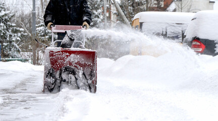 A man with a snow blower removes snow in the yard of a house