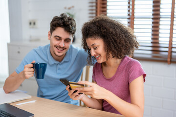 Latina couple using smartphone shopping online in living room at home. 