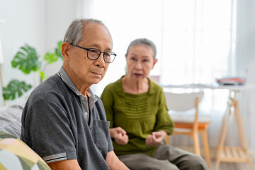 Asian senior couple sitting on sofa with painful after fight argument. 