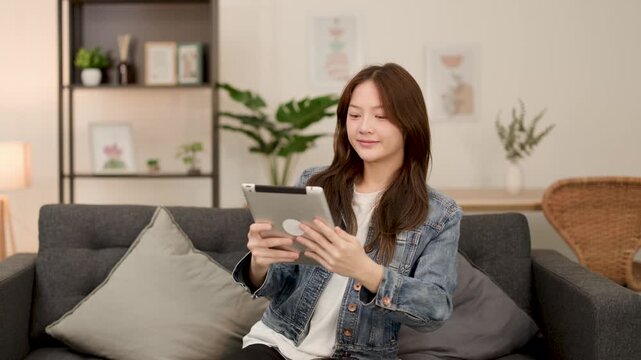 Young Asian woman relaxing on sofa using digital tablet