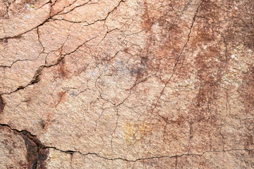 Close-up of natural stone surface texture with cracks and weathered details. Abstract rocky background showing aged mineral patterns and rough stone structure.