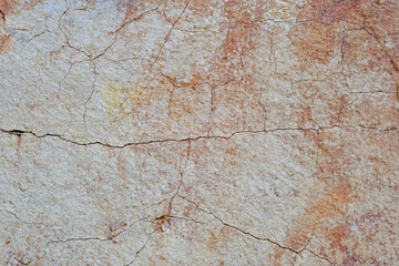 Close-up of natural stone surface texture with cracks and weathered details. Abstract rocky background showing aged mineral patterns and rough stone structure.