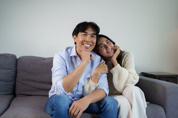 Obraz premium Happy asian couple smiling sitting together on sofa