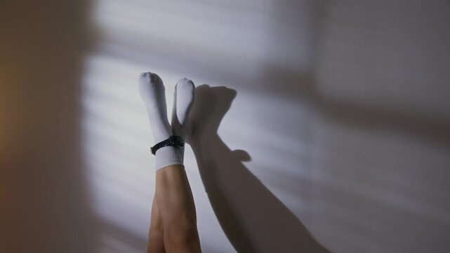 Unrecognizable pair of crossed bare female legs, wearing white socks and house arrest bracelet, raised against wall