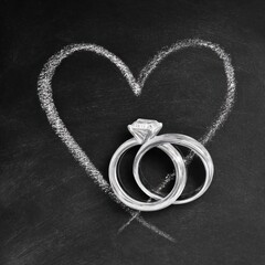 Two chalk-drawn wedding rings with a diamond inside a heart shape on a blackboard background.