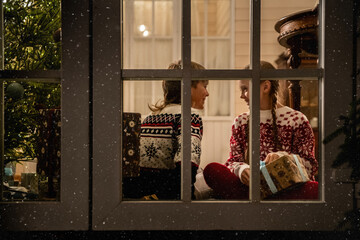 Two children celebrating Christmas at home, view through window
