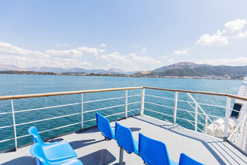 Empty blue seats on ferry deck with sea and coastal mountains view