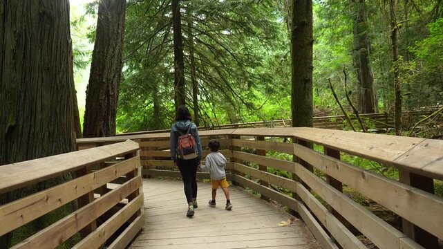 Mother and son enjoy a leisurely stroll along a wooden boardwalk, surrounded by the towering trees of cathedral grove nature park on vancouver island