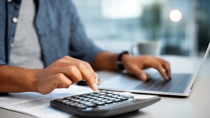 A professional is working on financial tasks, entering numbers on a calculator while referencing a laptop. The scene highlights productivity, accuracy, and digital workflow in an office setting