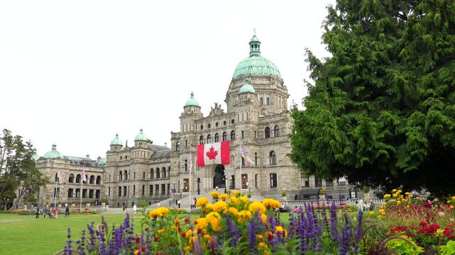 Flowerbeds enhance the majestic british columbia parliament buildings, proudly displaying the canadian flag, in the heart of victoria, british columbia