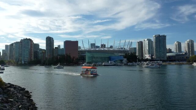 Vancouver passenger ferry cruising near bc place stadium, revealing waterfront skyline against bright, cloudy sky while navigating false creek's urban maritime landscape