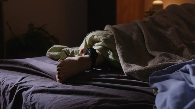 Unrecognizable woman, wearing house arrest ankle bracelet, sleeping in bed covered with blanket