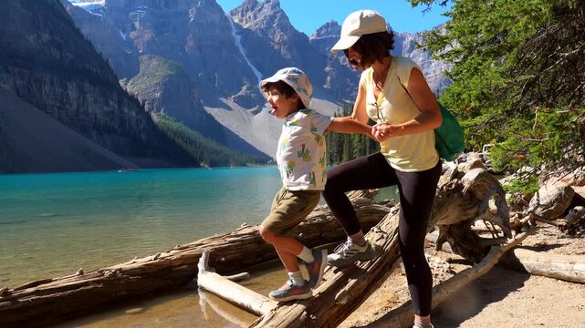Happy mother and son carefully balancing on a log at the edge of beautiful moraine lake in banff national park, with stunning turquoise water and mountain backdrop