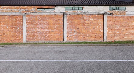 Wall with hollow brick exposed of old abandoned industrial building Strip of grass and road in front. Background for copy space