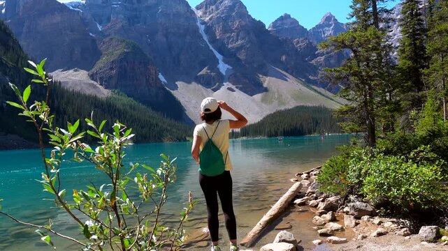 Majestic mountains surround a crystal clear turquoise lake, where a young woman stands on the shore, captivated by the breathtaking beauty of moraine lake in banff national park, alberta, canada