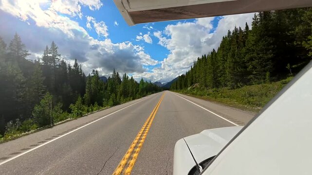 White motorhome driving on a scenic highway through the canadian rockies, offering breathtaking views of the mountains and forest landscape under a summer sky