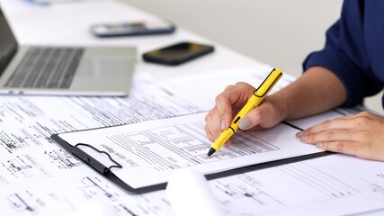 Close up hand of Architect or engineer hand holding pen working on blueprint construction floor plans on desk with engineering tools.