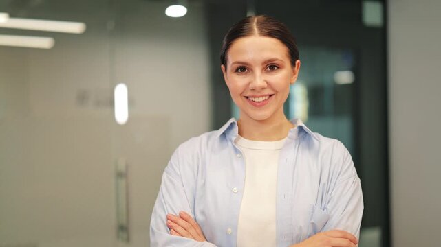 Confident woman stands in modern office, smiling genuinely. Expresses happiness, success, professionalism. Pose conveys self-assurance, ready for business challenges.