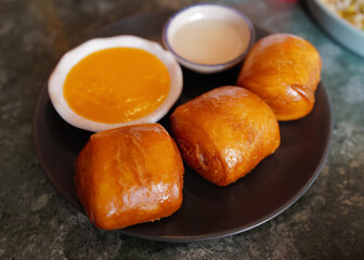Close up deep fried bun served with salted egg sauce and sweet condensed milk