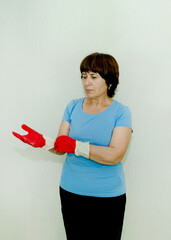 Elderly woman puts on bright red rubber gloves, preparing to clean house, protect her hands from cleaning products.