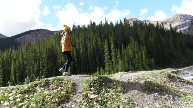 Young woman wearing an orange jacket and yellow hat walks along the ci fuentes path, enjoying the stunning views of the canadian rockies and the turquoise water of the sunwapta river