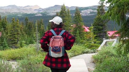 Backpacker walking on a wooden path towards num ti jah lodge at bow lake in banff national park, surrounded by lush vegetation and stunning mountain views