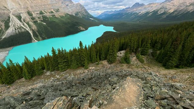 Turquoise waters of peyote lake surrounded by evergreen forests and rocky mountains, with hiker navigating rugged terrain capturing pristine canadian rockies landscape