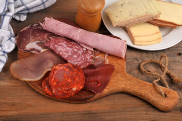Assortiment de charcuteries sur une planche &agrave; d&eacute;couper en bois avec une assiette de fromages &agrave; raclette