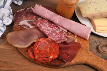 Assortiment de charcuteries sur une planche &agrave; d&eacute;couper en bois avec une assiette de fromages &agrave; raclette