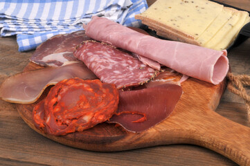 Assortiment de charcuteries sur une planche à découper en bois avec du fromage à raclette tranché