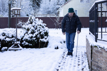 Elderly man stepping out of parked car using cane, winter conditions, residential driveway with snow and cobblestones.