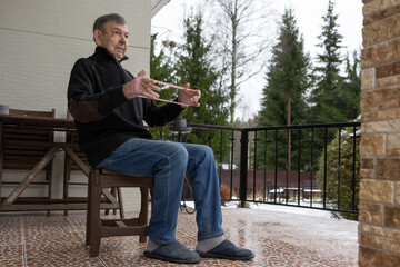 Senior male performing light rehabilitation exercise with elastic band at home patio in winter season supporting mobility balance daily wellness.